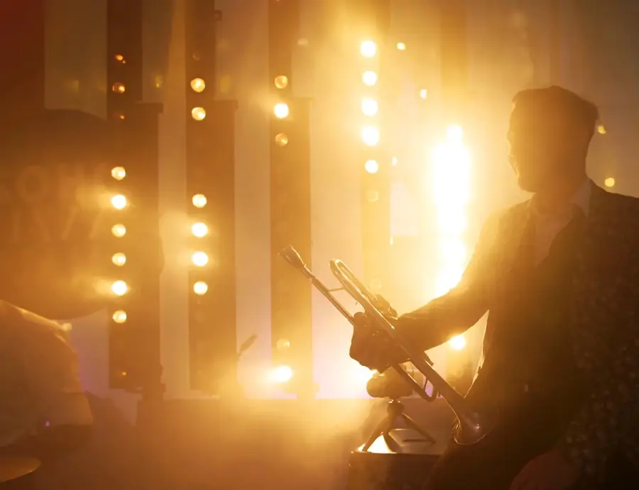 A horn player in silhouette against gold stage lights