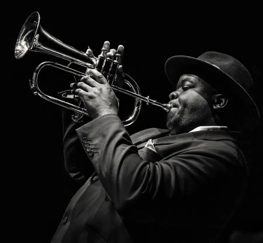 Marvin Mouneké playing trumpet in a hat, lit from the side