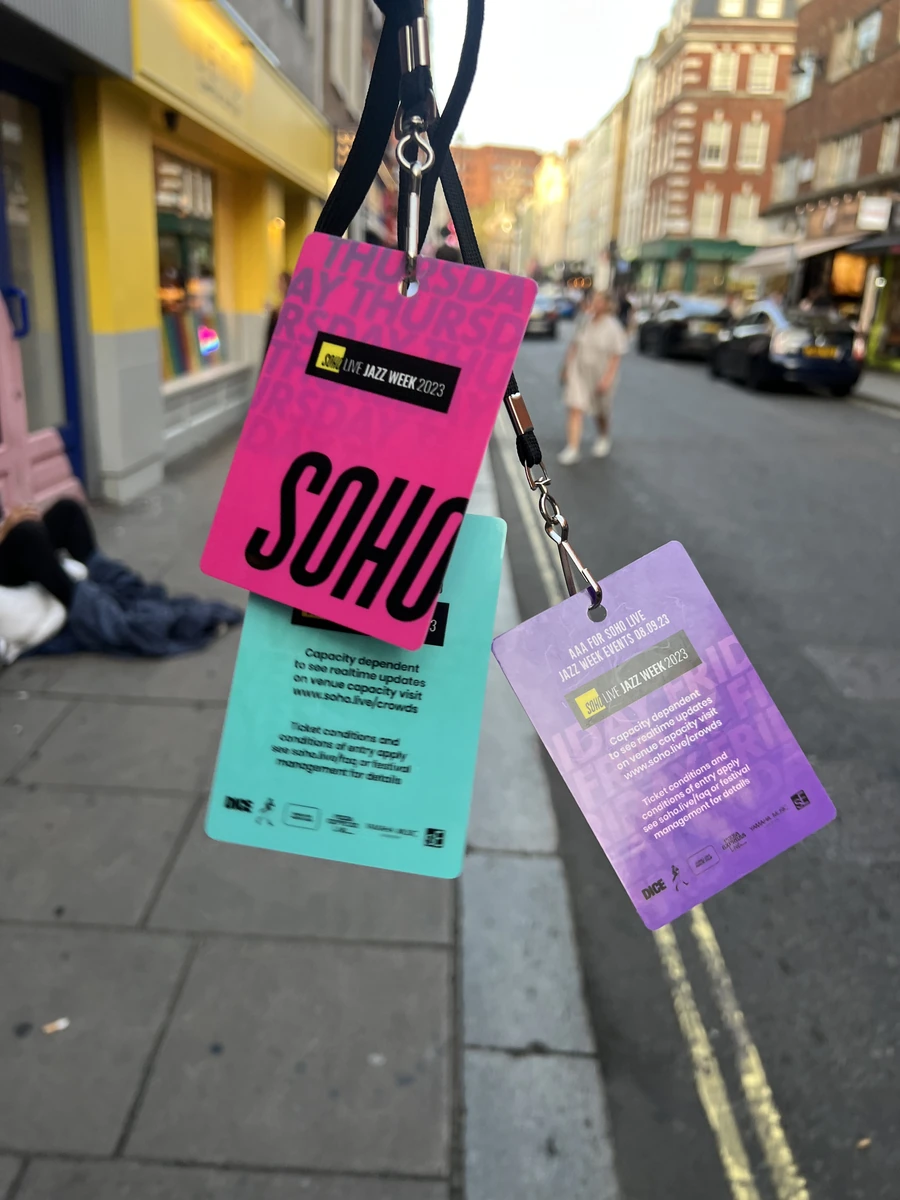 Magenta, turquoise and lilac Soho Live Jazz Week 2023 passes hanging from lanyards on a Soho street