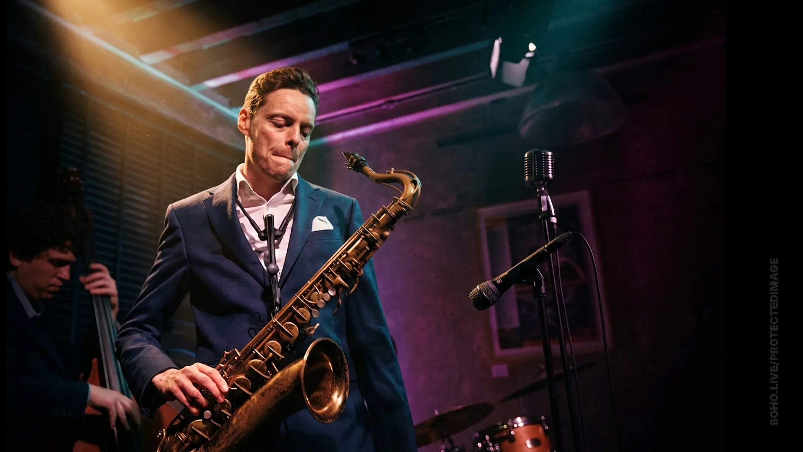 Fraser Smith playing saxophone on a club stage, the mark set into the right edge of the frame.